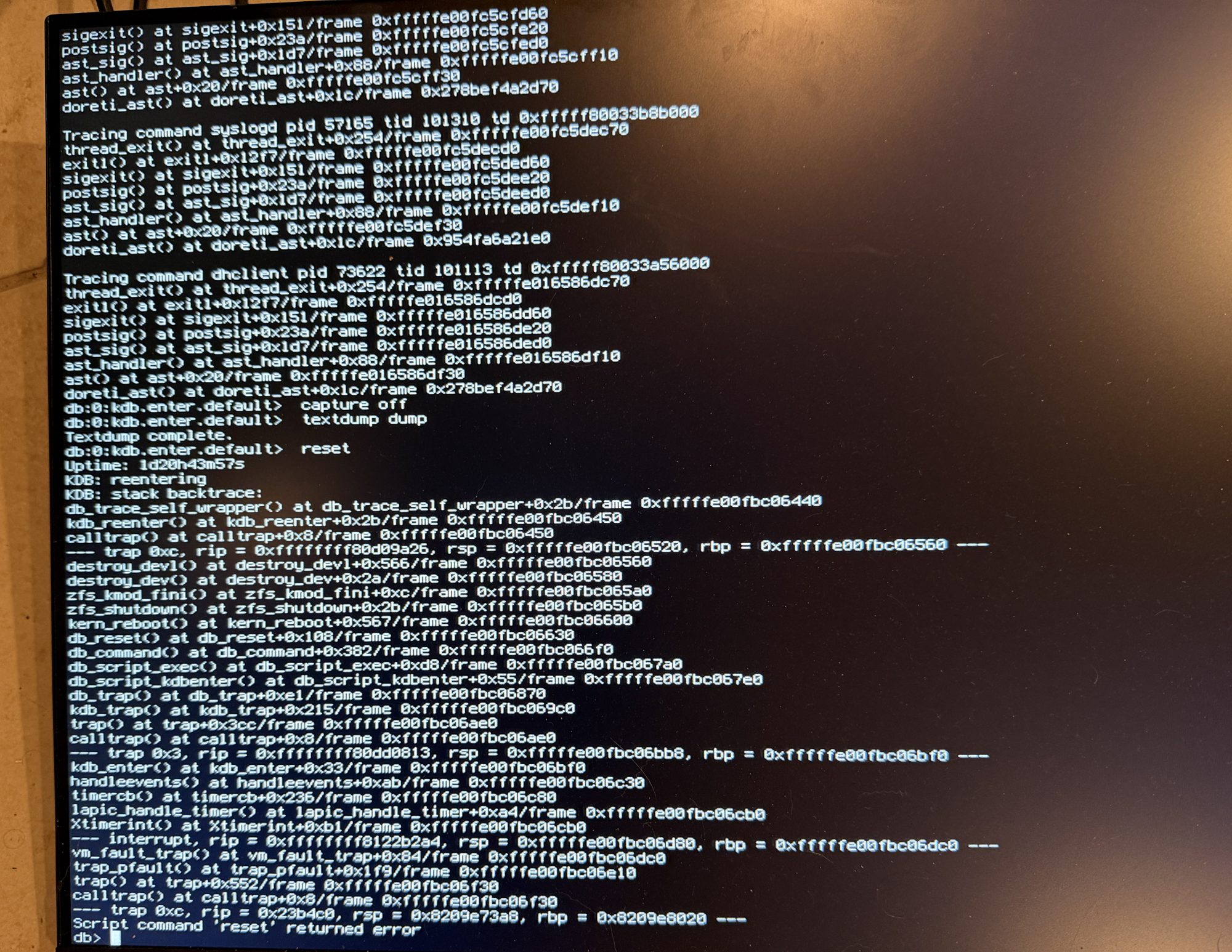 The firewall's console wedged in the kernel debugger: the death traces of syslogd and dhclient at the top, the textdump sequence completing, and then KDB re-entering when the reset command's own reboot path page-faulted, ending at a db> prompt